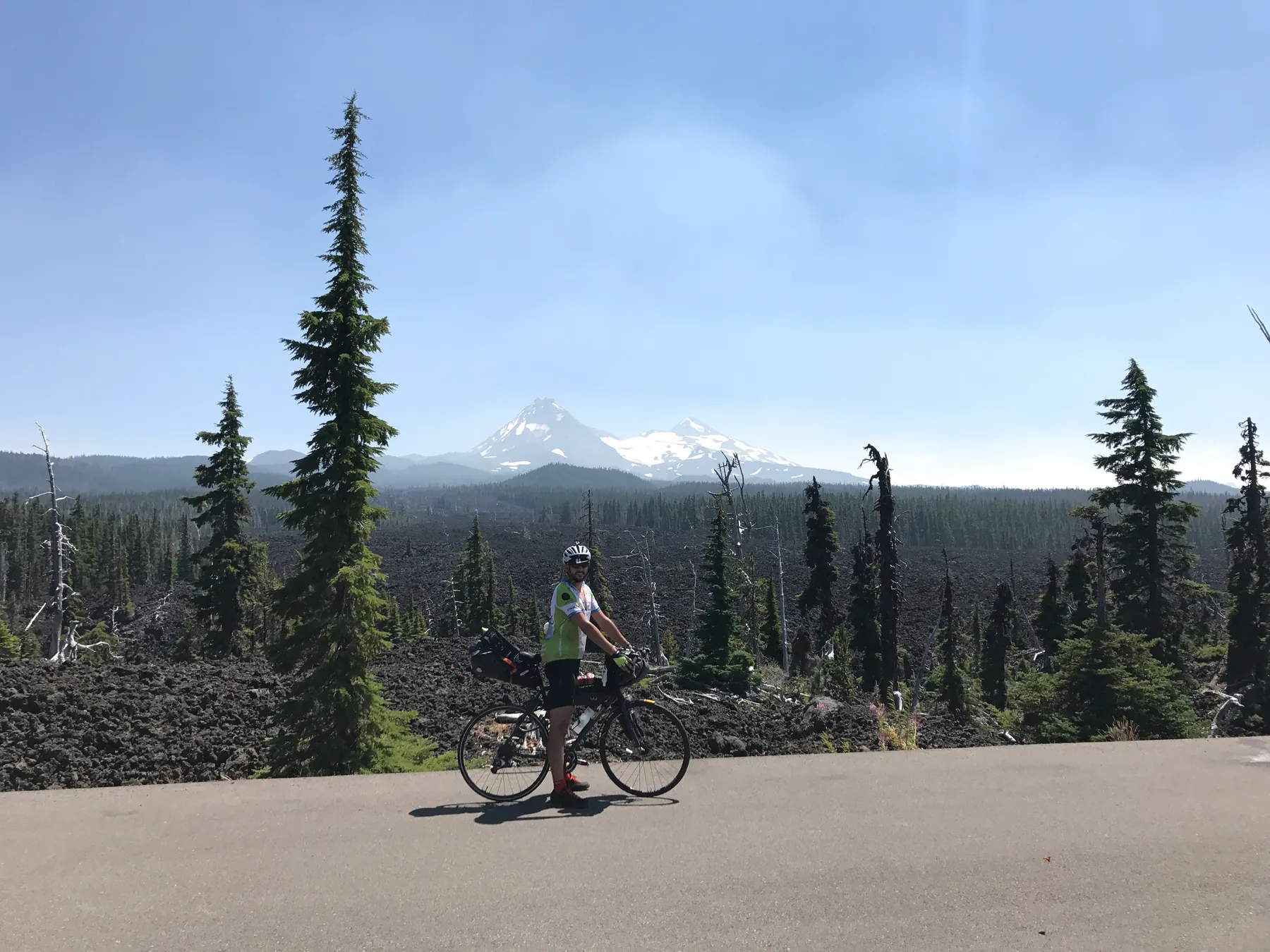 A cyclist with a loaded bike in front of mountains and dark lava fields in Oregon.
