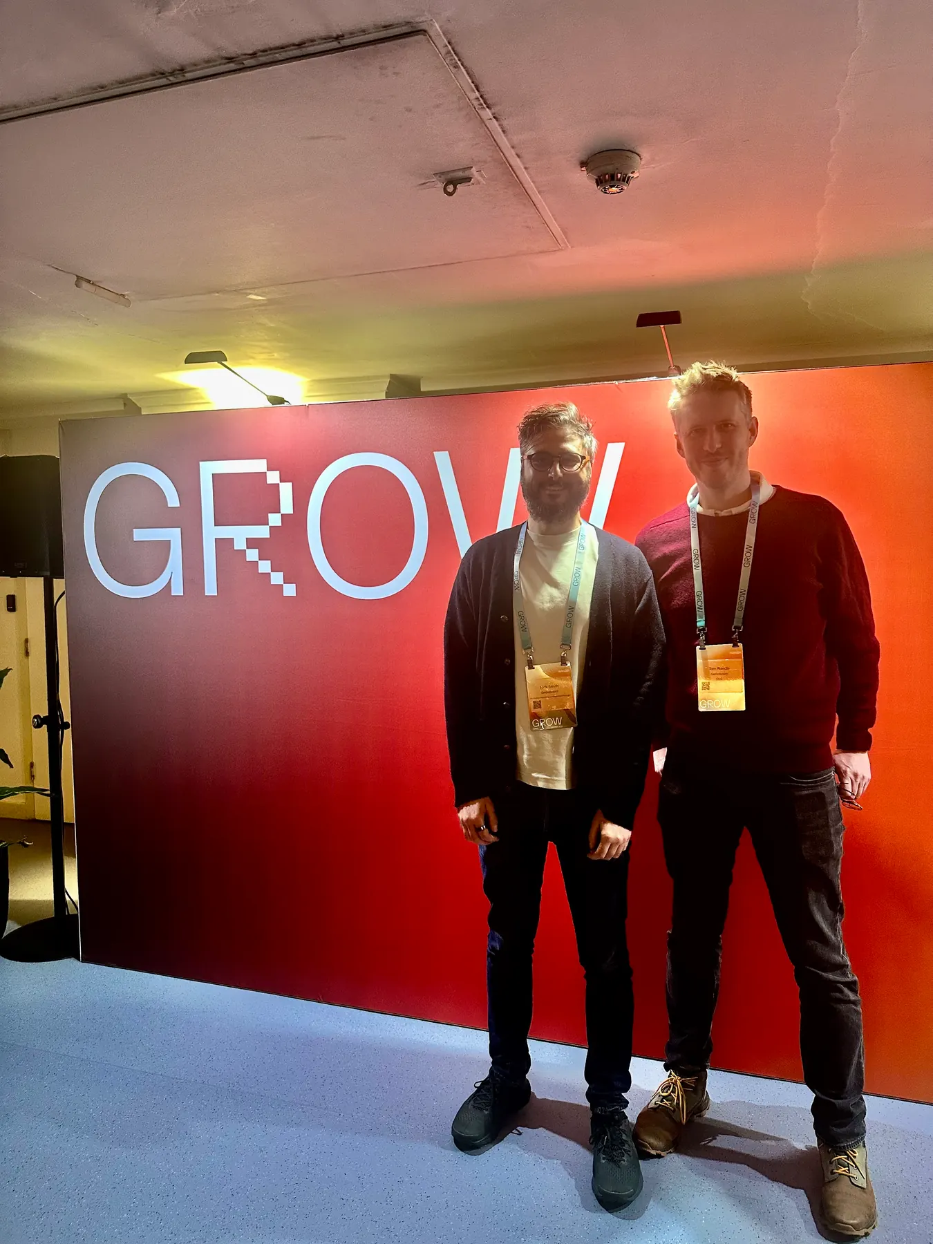 Two people standing in front of a red HubSpot Grow event wall.